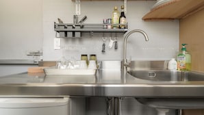 Una cucina con lavello in acciaio inox, lavastoviglie e piano di lavoro con diversi utensili da cucina e bottiglie.
