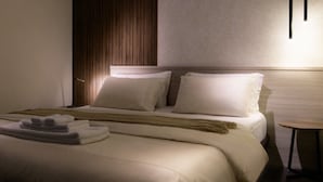 Una camera d'albergo con un letto, cuscini, un comodino e una lampada.