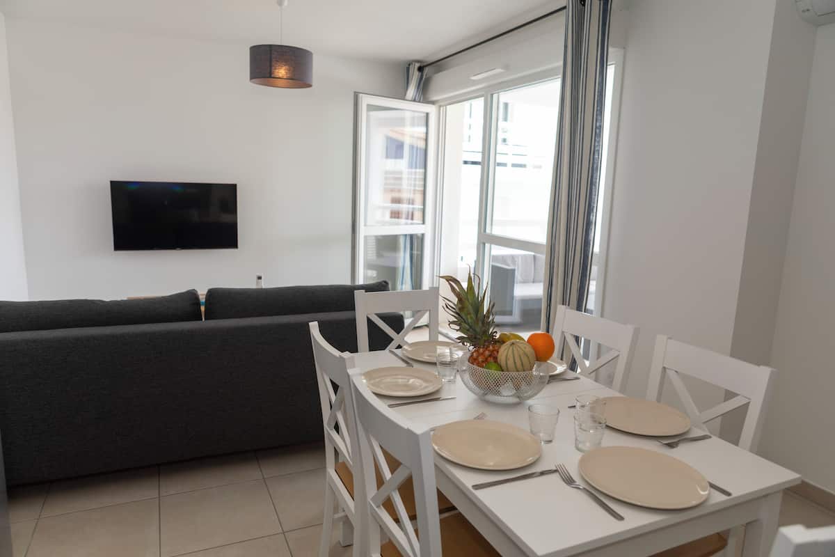 Ein modernes Wohnzimmer mit einer Couch, einem Esstisch für zwei Personen und einem an der Wand befestigten Flachbildfernseher.