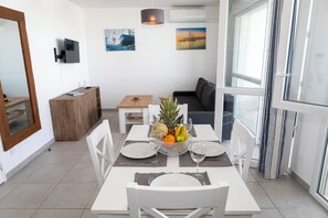 A dining area with a table set for four, a fruit bowl, and a sofa in the background. - MY Hôtel Résidences - Port Leucate  (Leucate)