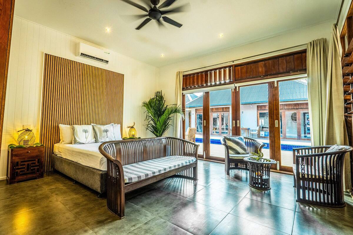 Une pièce spacieuse comprenant un lit, deux canapés, une petite table et une grande fenêtre donnant sur la piscine.