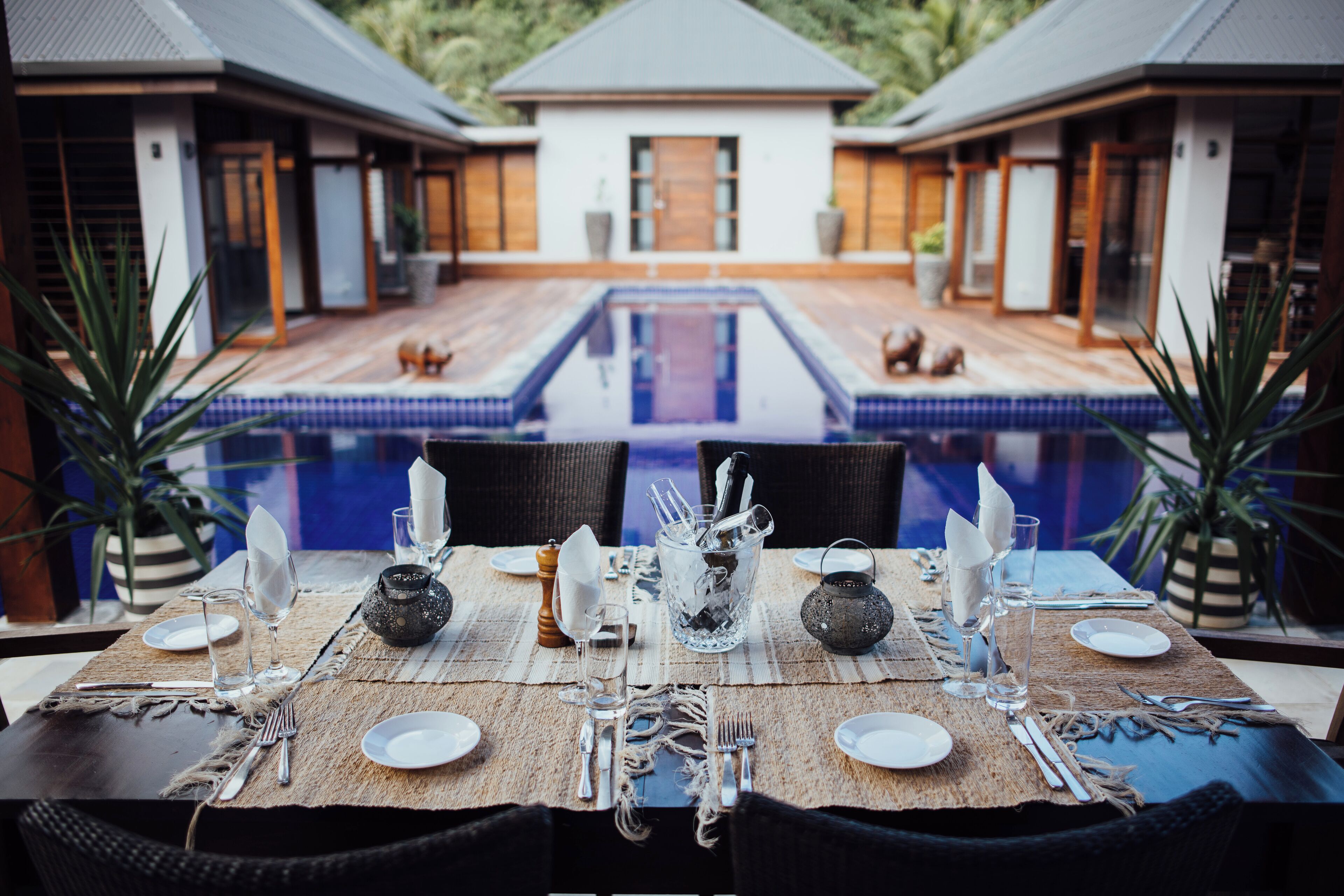 A dining table set for four with a view of a swimming pool and two houses in the background.