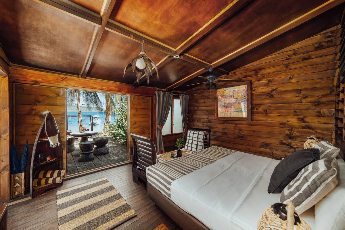 Une chambre dans un chalet en bois, avec un lit, une vue sur l’extérieur et un ventilateur de plafond.