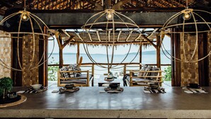 A dining area with a view of the sea, featuring a wooden ceiling, hanging light fixtures, and a rustic seating arrangement. - Trees and Fishes Private Retreat (Port-Havannah)