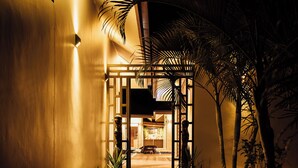 A pathway leading to a building entrance with a modern design, a well-lit entrance area, and surrounding tropical plants. - Trees and Fishes Private Retreat (Port-Havannah)