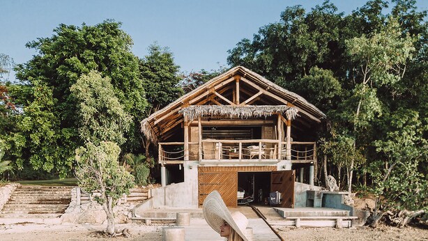 A woman sitting on a dock with a house in the background. - Trees and Fishes Private Retreat (Port-Havannah)