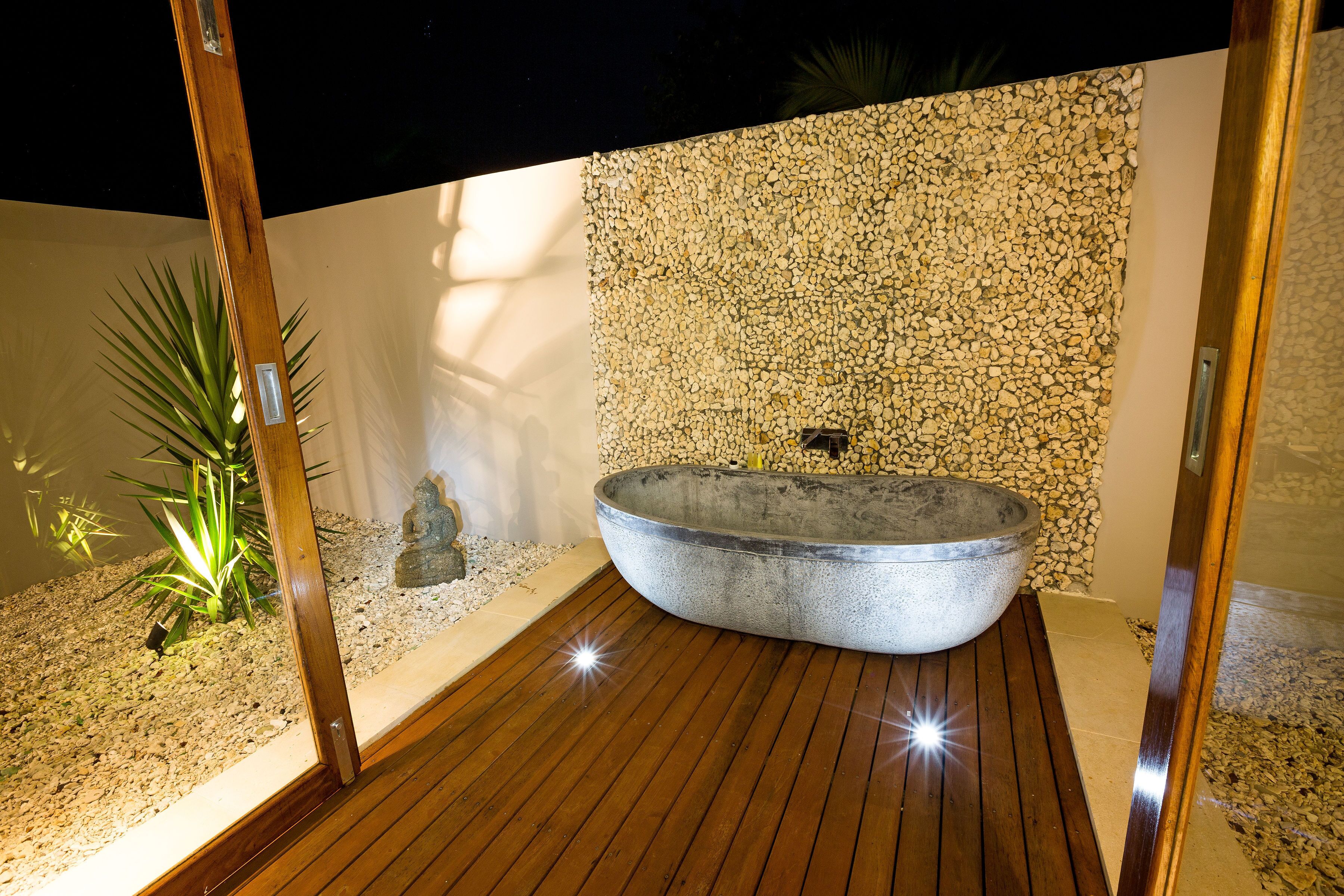 Un baño moderno con una bañera independiente, piso de madera y una pared de piedras.