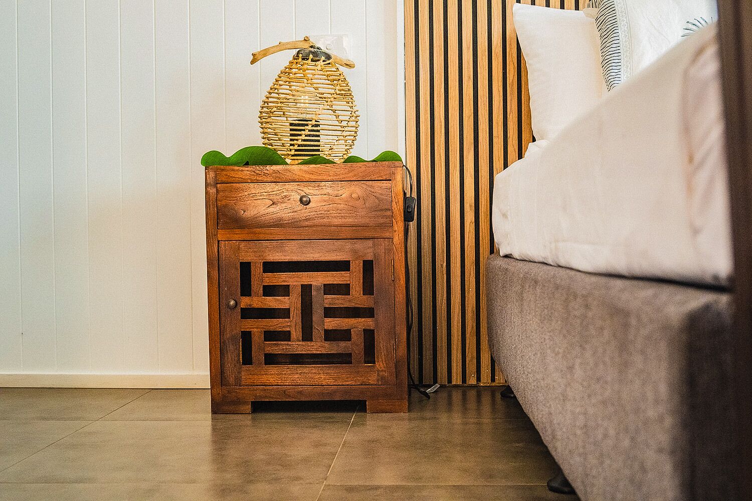 Una mesita de noche de madera con una cesta tejida encima, un cajón y una planta pequeña.