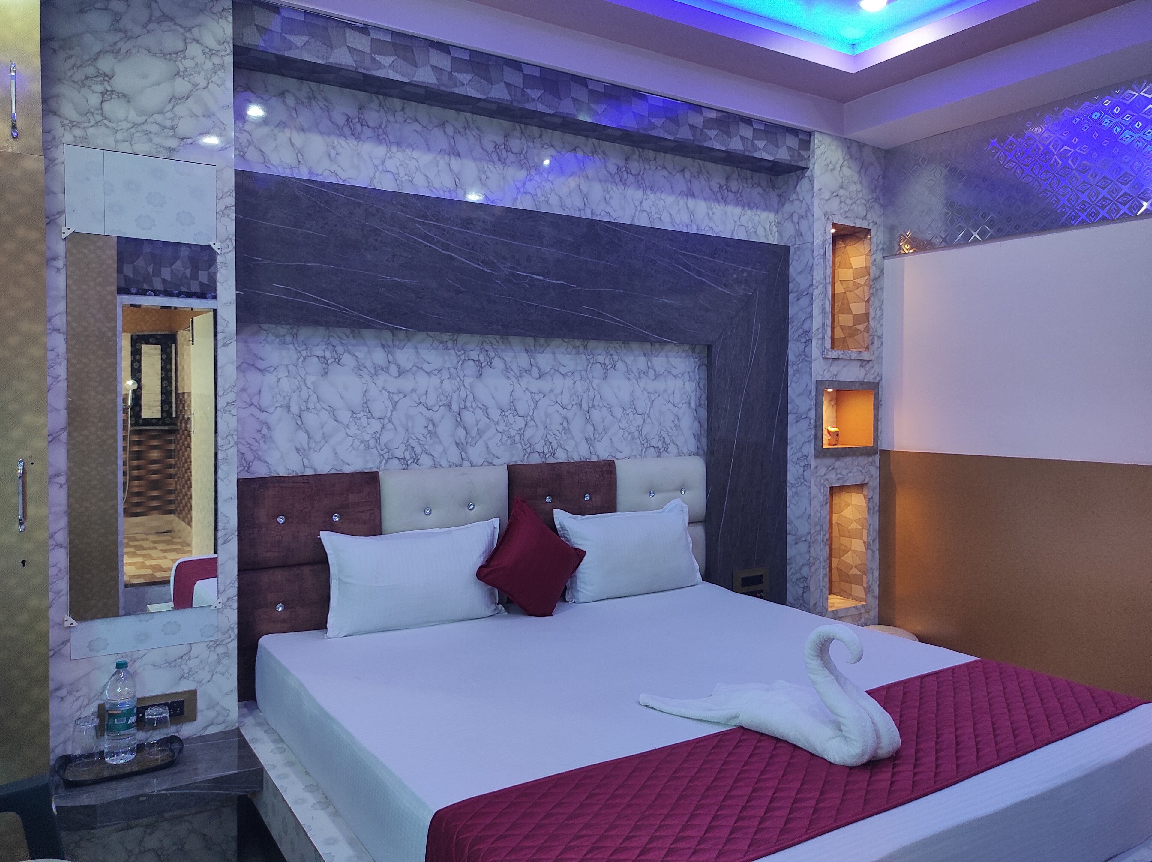 Habitación de hotel con cabecera de mármol, cama con colcha roja y toalla con forma de cisne.