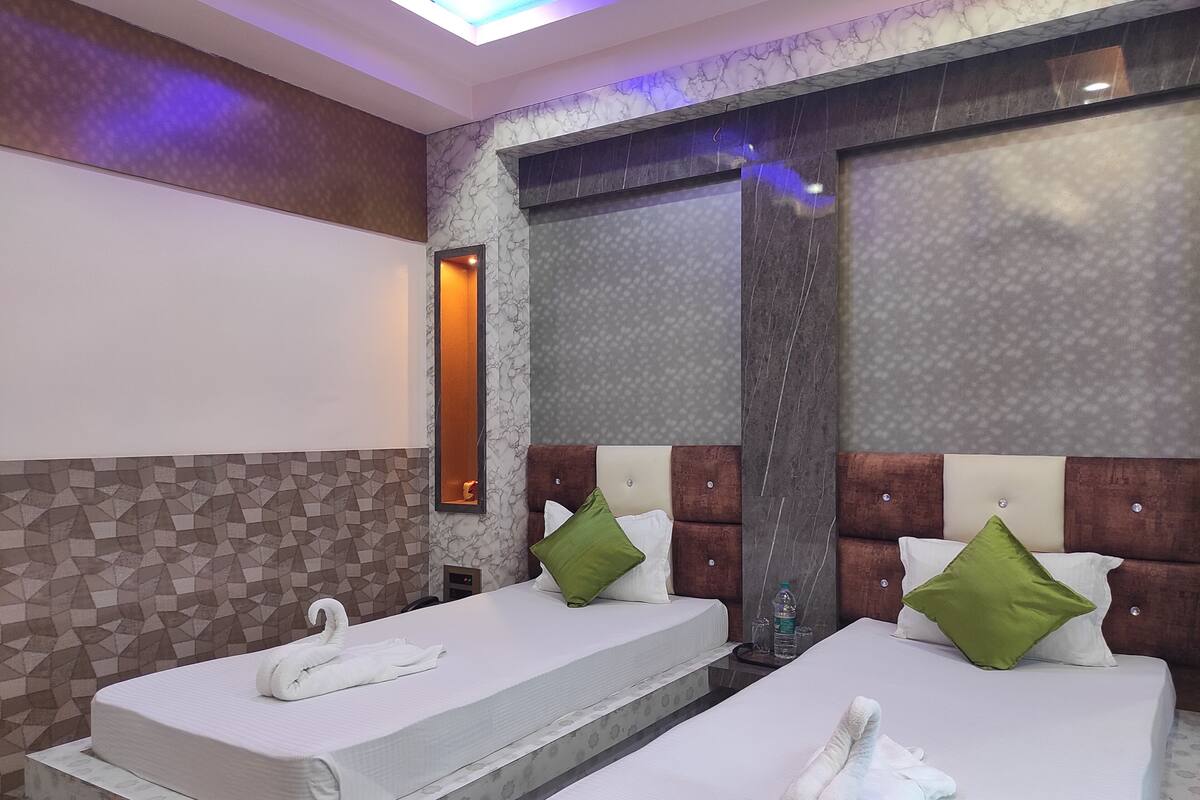 A hotel room with two beds, each with a towel and pillow, a mirror, and a patterned wall.