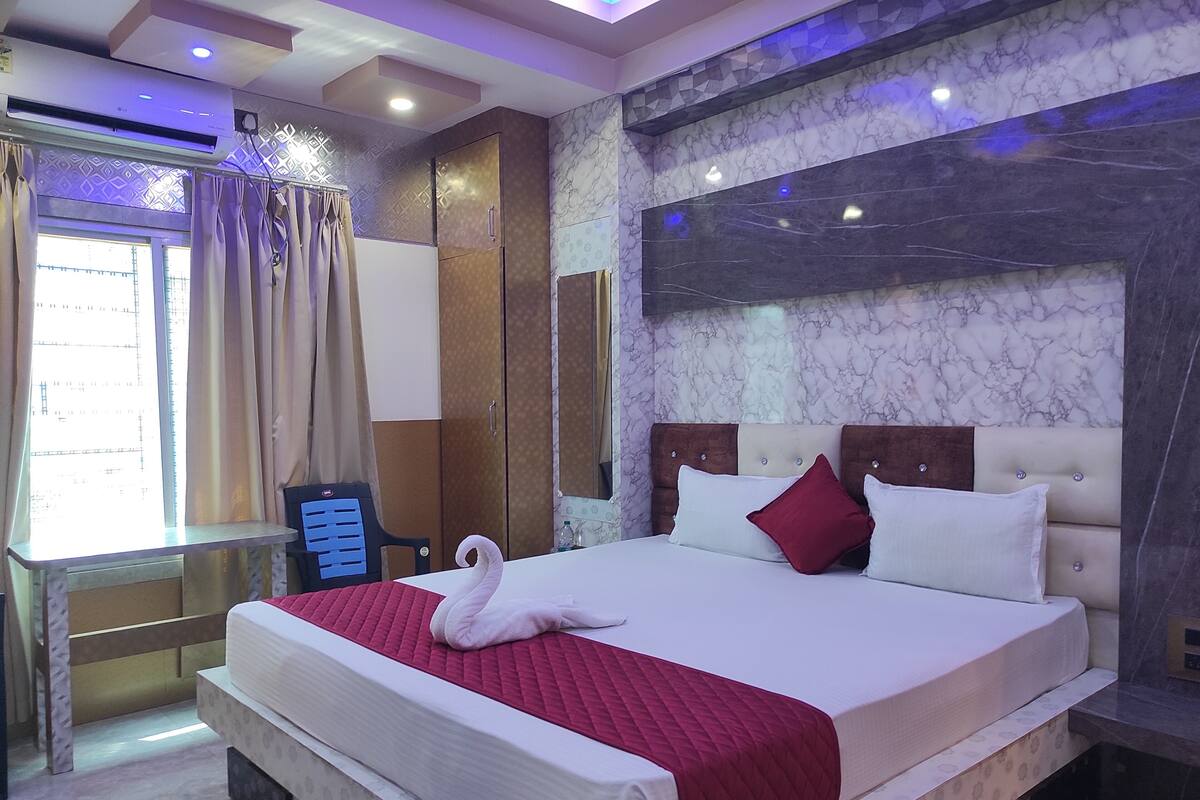 A hotel room with a large bed, a wardrobe, a desk, and a window with curtains.