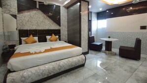 Una habitació d'hotel moderna amb un llit gran, una zona de seients amb taula i cadires, i un ventilador de sostre.