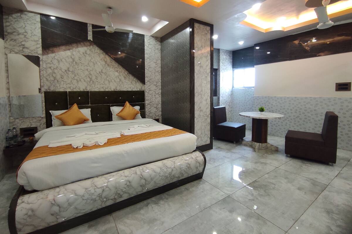 A modern hotel room with a large bed, a sitting area with a table and chairs, and a ceiling fan.