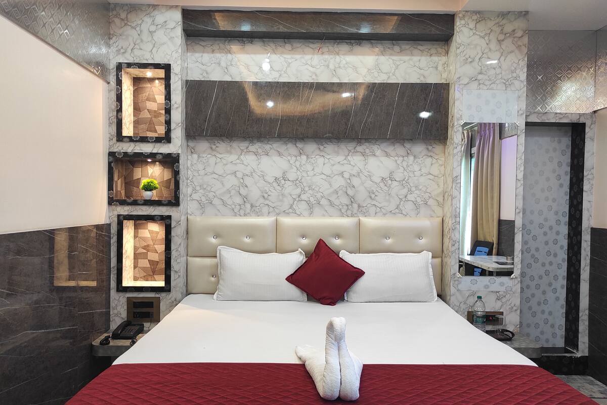 A modern hotel room with a marble-patterned wall, a tufted headboard, and a red accent pillow.