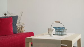 A room with a red sofa, a small table with a white vase and a glass container, and a white wall. - Apartment in Luxury Residence - Ostuni the White City (Ostuni)