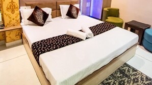 A hotel room with a large bed, patterned wallpaper, a ceiling fan, and a green chair. - Hotel 7PM (Shaheed Bhagat Singh Nagar)