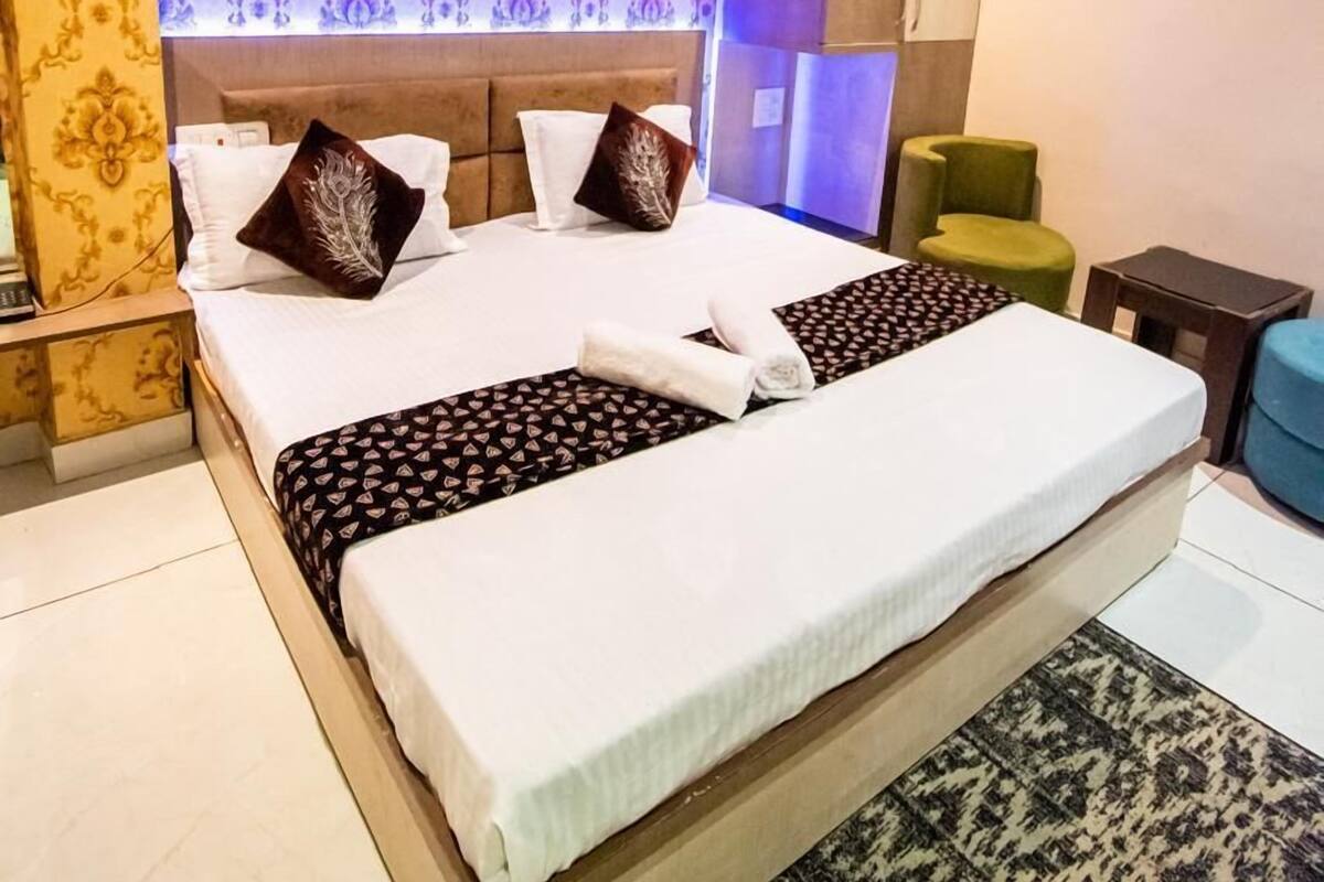 A hotel room with a large bed, patterned wallpaper, a ceiling fan, and a green chair.
