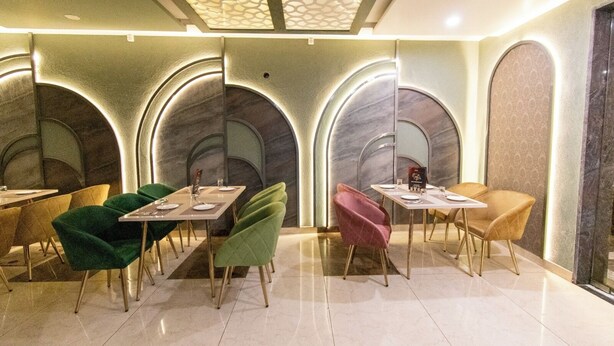 A modern restaurant with a unique arched ceiling design and a variety of seating options including green and pink chairs. - Hotel 7PM (Shaheed Bhagat Singh Nagar)