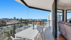 Een balkon met een witte tafel en stoelen, een bank, en uitzicht op de stad en zee.