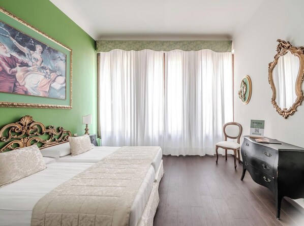 A hotel room with a bed, a chair, a dresser, a painting, and a window with curtains. - Hotiday Room Collection - Venezia Santa Lucia (Venice)