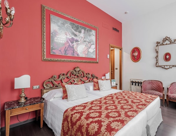 Una habitación de hotel con una cama grande, una mesita de noche, un escritorio, una silla y un cuadro en la pared.