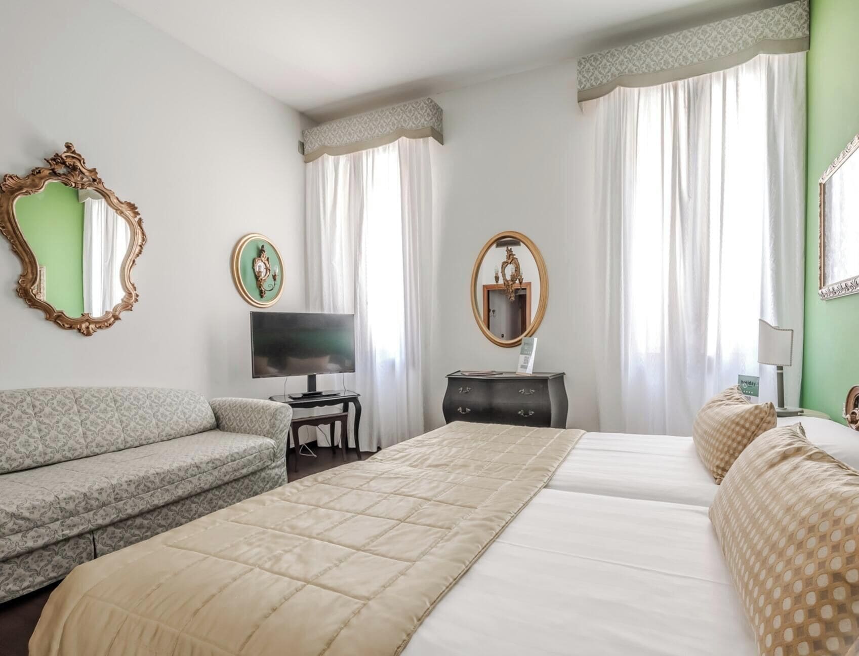 Una camera d'albergo con un letto, un divano, una TV e un comò.