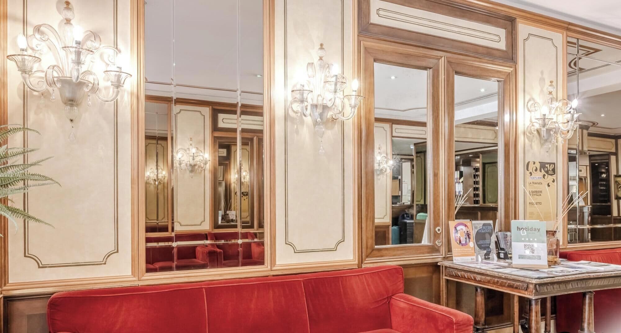 Un'elegante hall d'albergo con sedute rosse, lampadari e pareti a specchio.