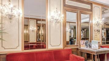 Un'elegante hall d'albergo con sedute rosse, lampadari e pareti a specchio.