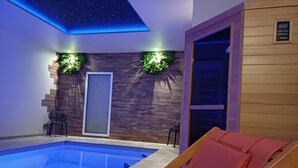 Area piscina interna moderna con soffitto a stelle, pareti in legno e una poltrona reclinabile rossa.