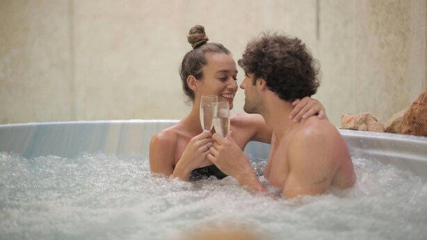 Due persone in vasca idromassaggio con bolle, che sorseggiano bicchieri.