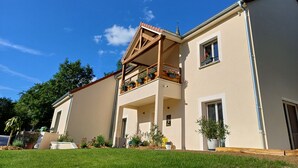 Una casa a due piani con un balcone, un piccolo giardino e un cielo azzurro intenso.