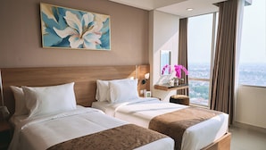 Habitación de hotel con dos camas, un ventanal con cortinas, un cuadro en la pared y una mesita de noche con lámpara.