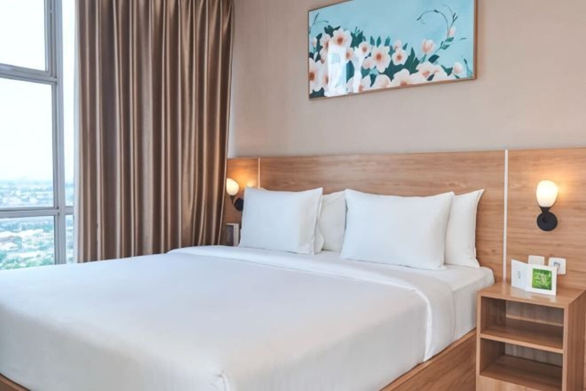 Une chambre d’hôtel avec un grand lit, une tête de lit en bois, deux lampes de chevet, une table de chevet et un tableau au mur.