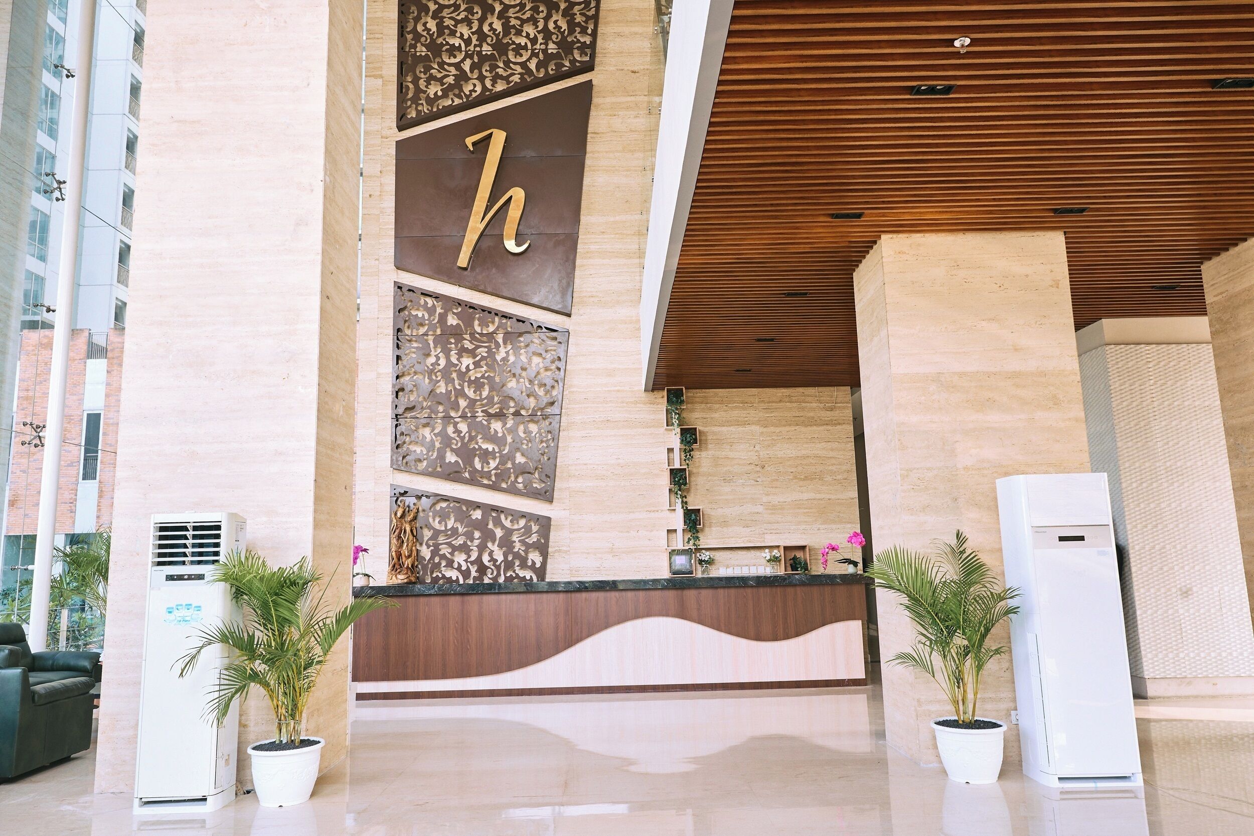 A hotel reception area with a modern design, featuring a large 'h' on the wall, a reception desk, and two air conditioning units.