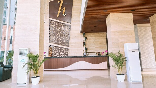 Un espace d’accueil d’hôtel au design moderne, avec un grand « h » sur le mur, un comptoir d’accueil et deux unités de climatisation.