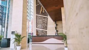 Un espace d’accueil moderne, doté d’un comptoir de réception en bois, de grands panneaux décoratifs et de plantes en pot.