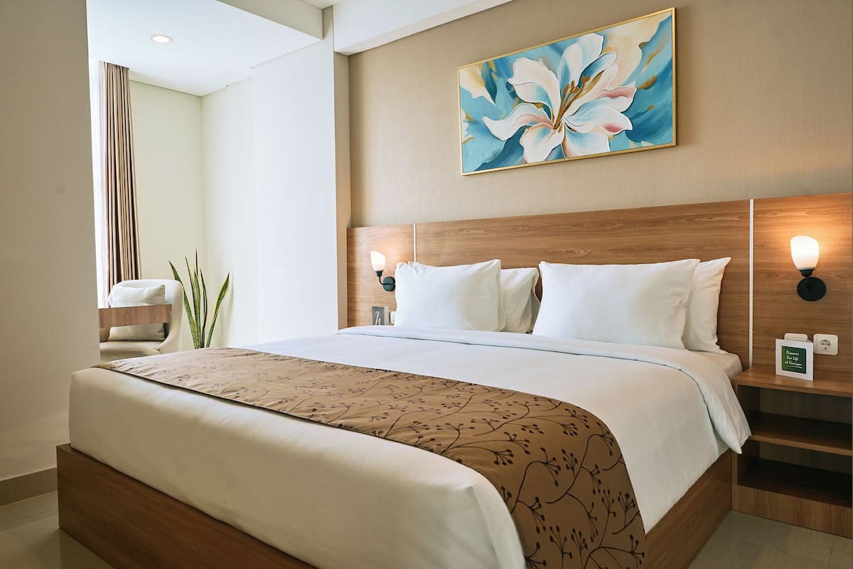 Una habitación de hotel con una cama grande, cabecero de madera, un cuadro colgado en la pared, lámparas de noche y una mesita de noche con lámpara.