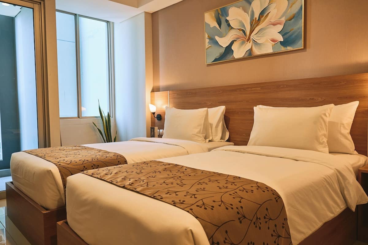 Habitación de hotel con dos camas, un ventanal grande y un cuadro de flores en la pared.