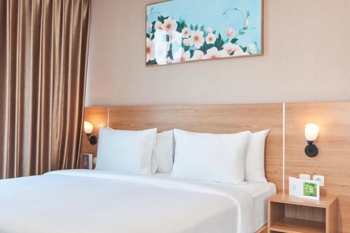 A hotel room with a bed, two bedside tables with lamps, a painting on the wall, and a curtain.