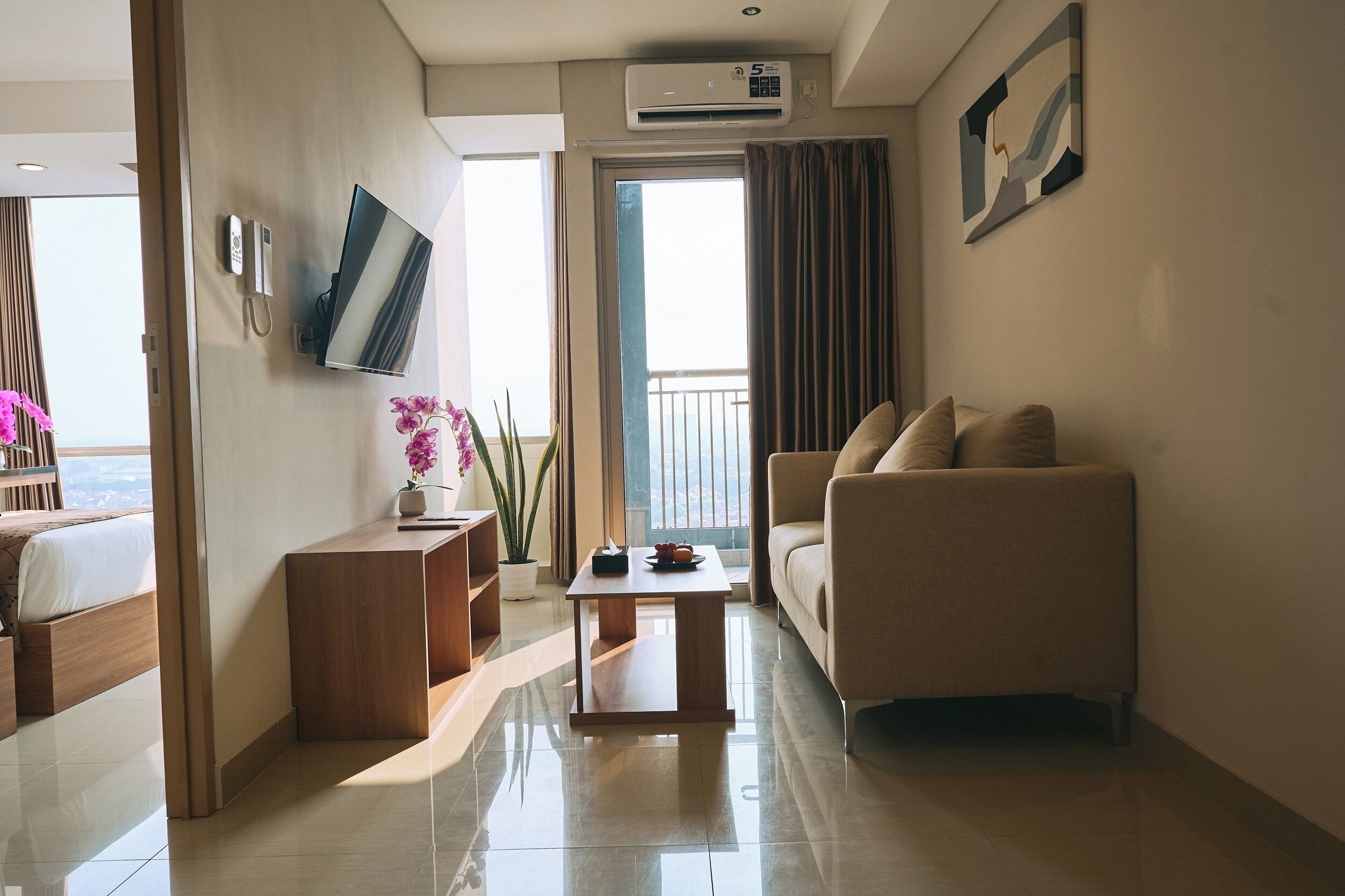 Ein modernes Hotelzimmer mit einer Couch, einem kleinen Holztisch, einem an der Wand montierten Fernseher und einem Balkon mit Vorhängen.
