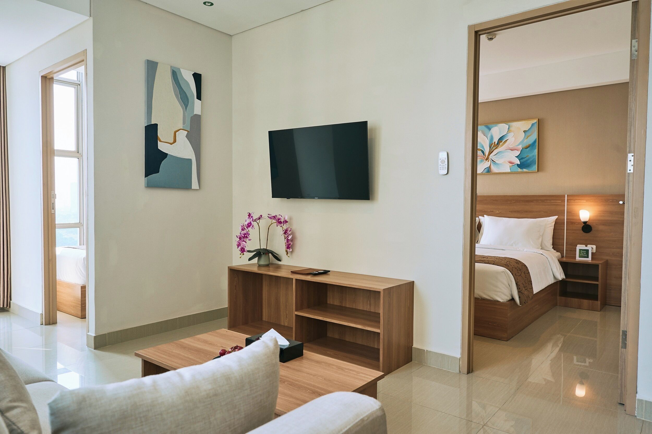 Ein modernes Hotelzimmer mit Flachbildfernseher, einem Holztischchen, einer Couch, einem Bett mit Holz Kopfteil und einem kleinen Nachttisch.