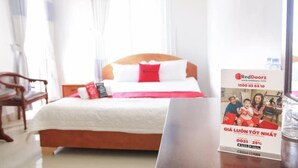 A hotel room with a bed, a wooden nightstand, and a poster on the wall.