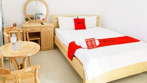 A hotel room with a wooden bed, a bedside table, a chair, and a small desk.