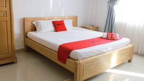 A neatly made bed with white and red bedding, a wooden headboard, and a small bedside table with a lamp.