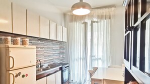 A modern kitchen with white cabinets, a built-in oven, and a dining area with a table and chairs. - Naples on foot (Napoli)