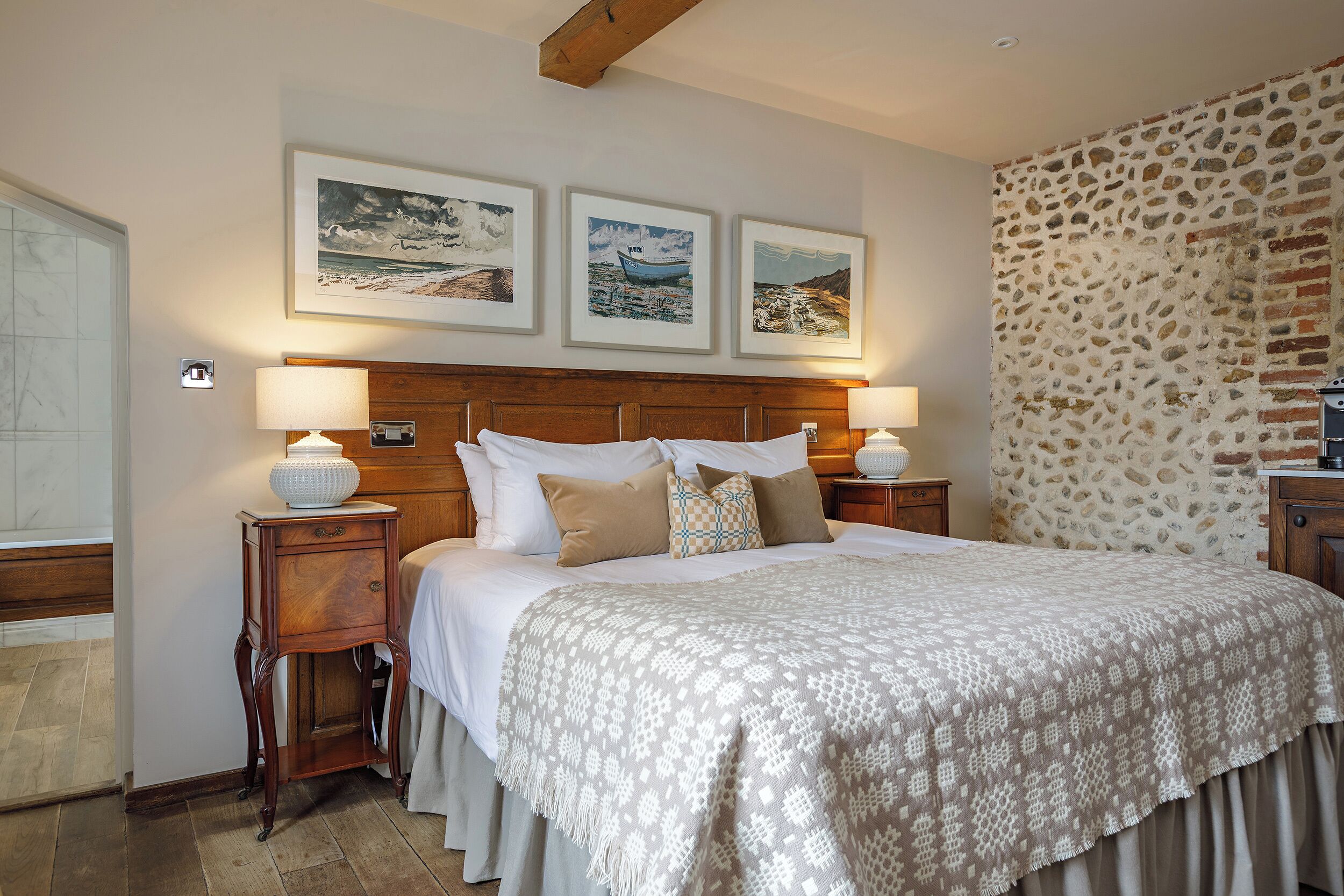 A neatly made bed with a patterned bedspread, two bedside tables with lamps, and three framed pictures on the wall above the bed.