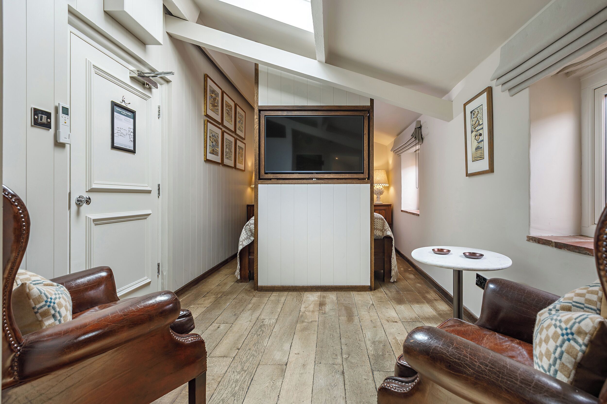 Un couloir étroit au plancher en bois, une porte blanche et une petite table sur laquelle reposent deux bols.