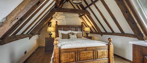 A rustic bedroom with a wooden bed, stone wall, and exposed wooden beams.