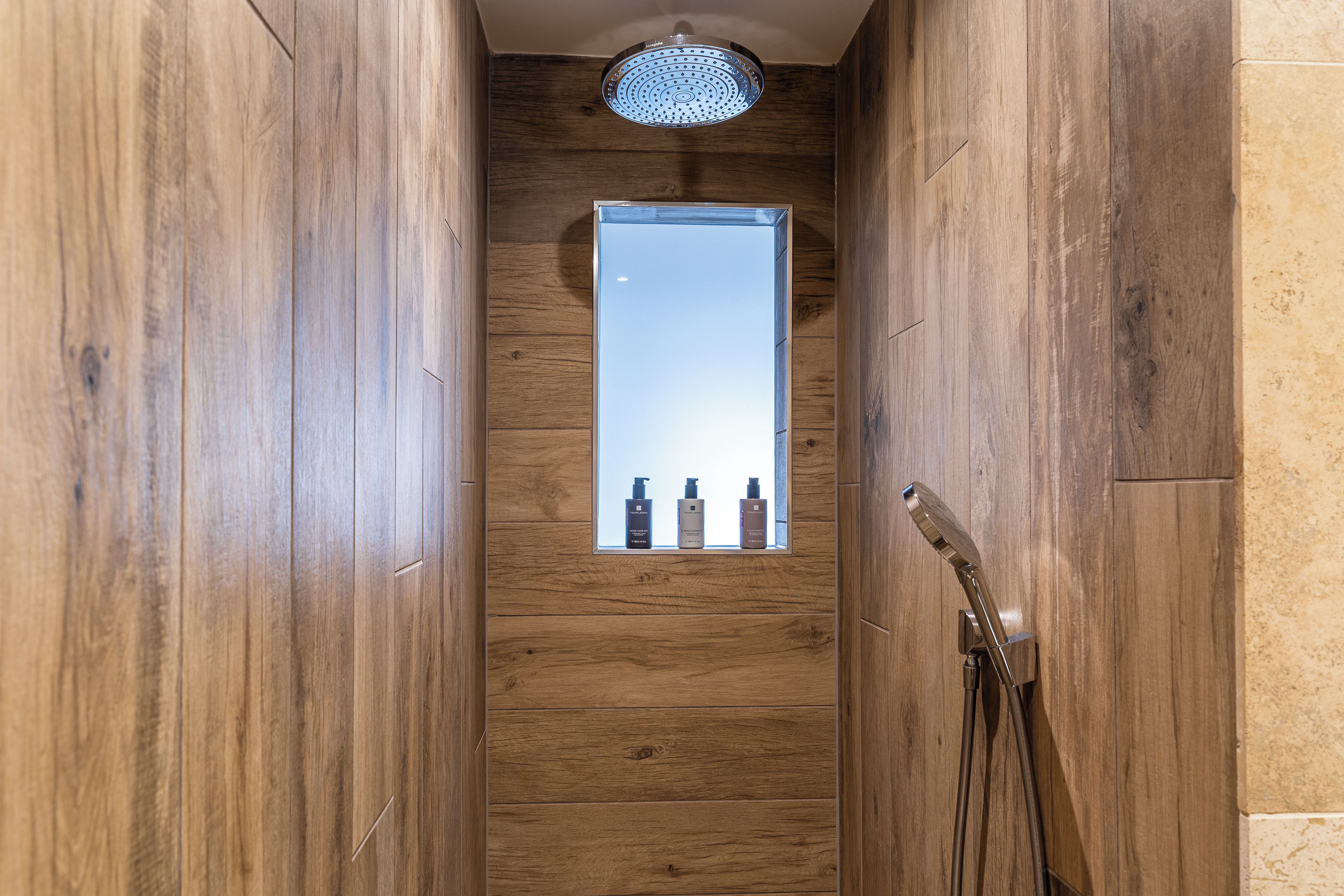 A narrow wooden hallway with a showerhead and a window displaying toiletries.