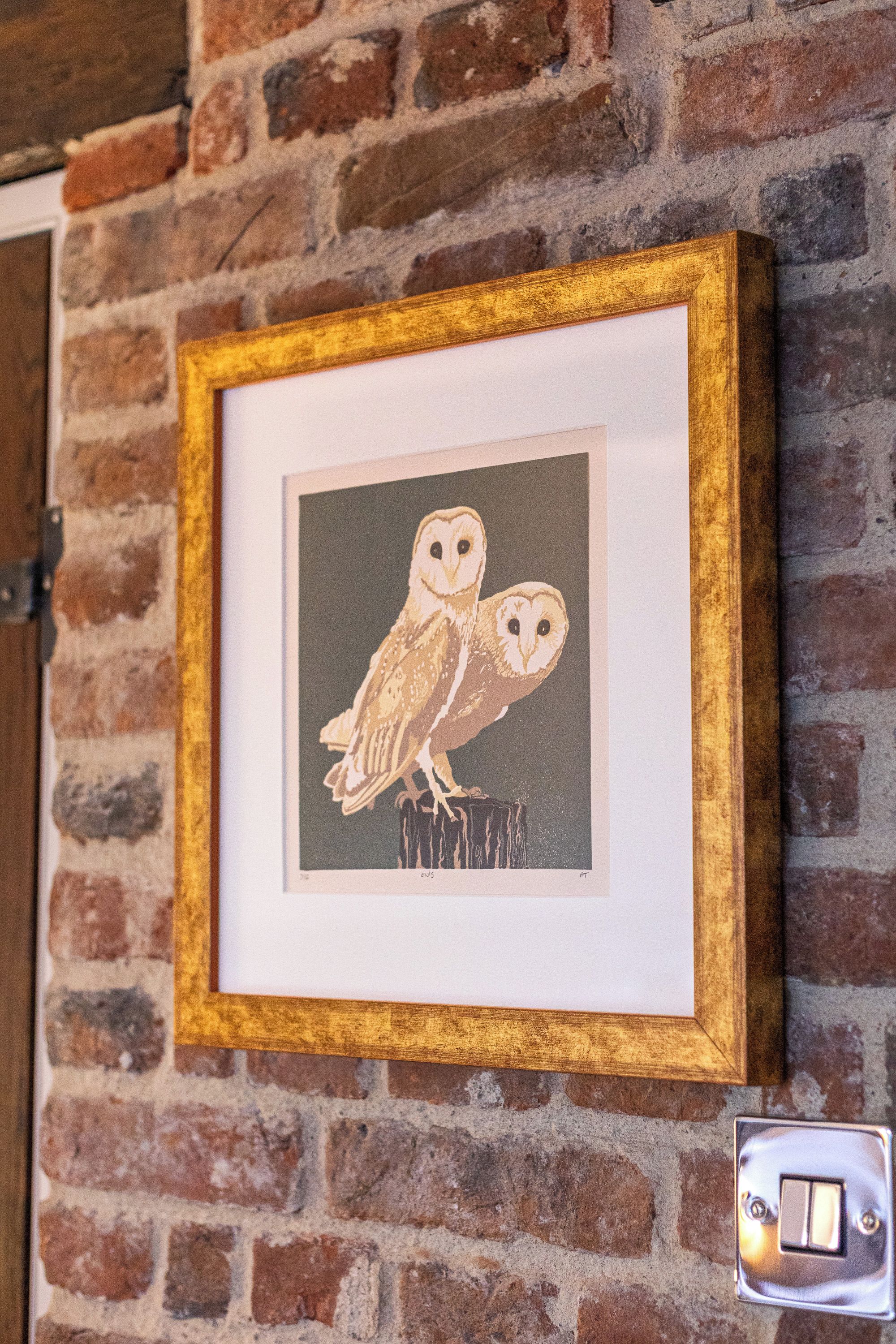 A framed artwork of two owls on a brick wall.